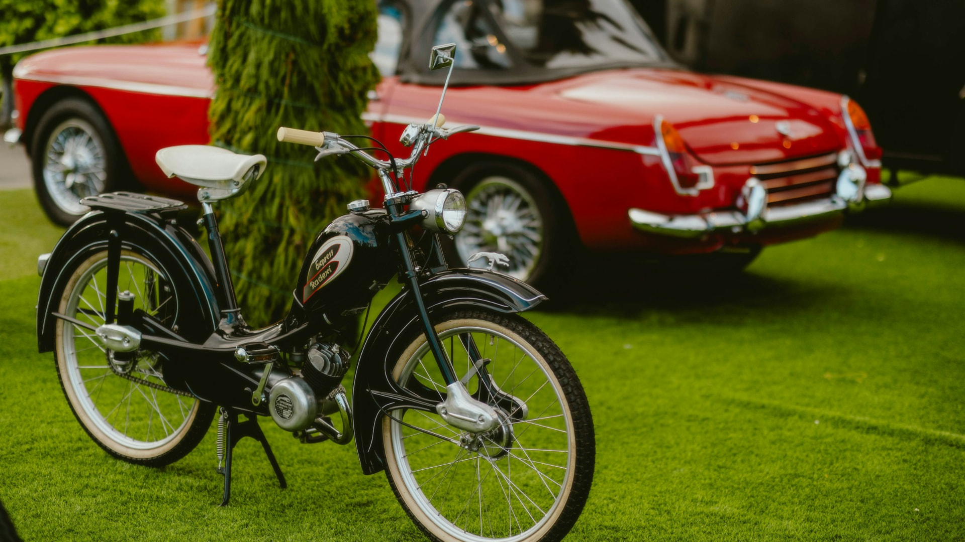 Zwarte Express bromfiets voor een rode klassieke sportwagen
