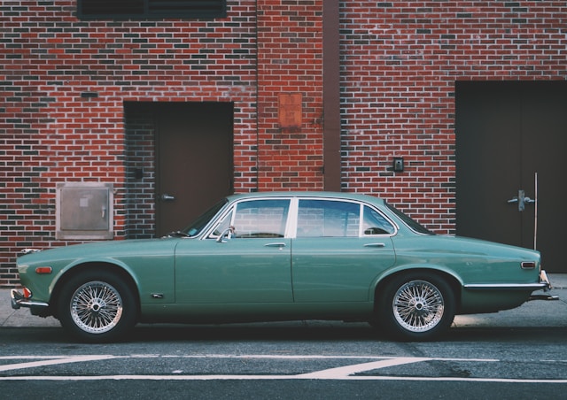 Groene klassieke Jaguar geparkeerd voor een bakstenen gevel